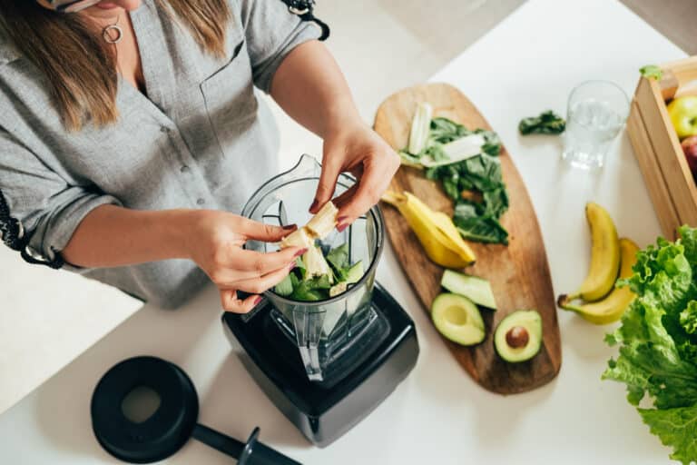 Woman is preparing a healthy detox drink in a blender a green smoothie with fresh fruits, green spinach and avocado. Healthy eating concept, ingredients for smoothies on the table, top view